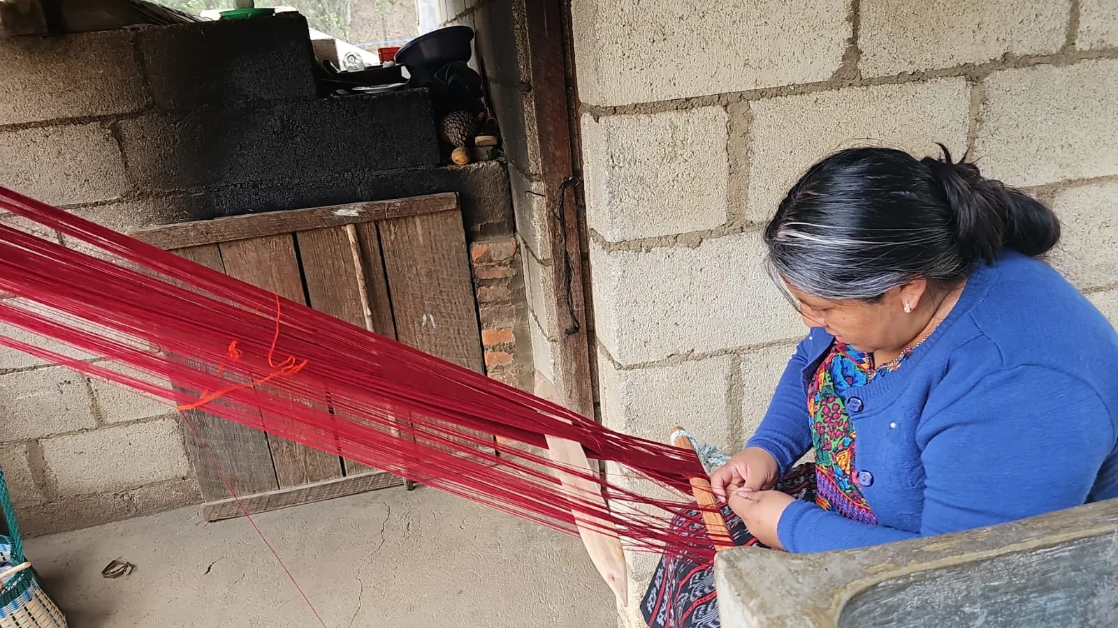 Tejedora preparando hilos rojos en telar de cintura